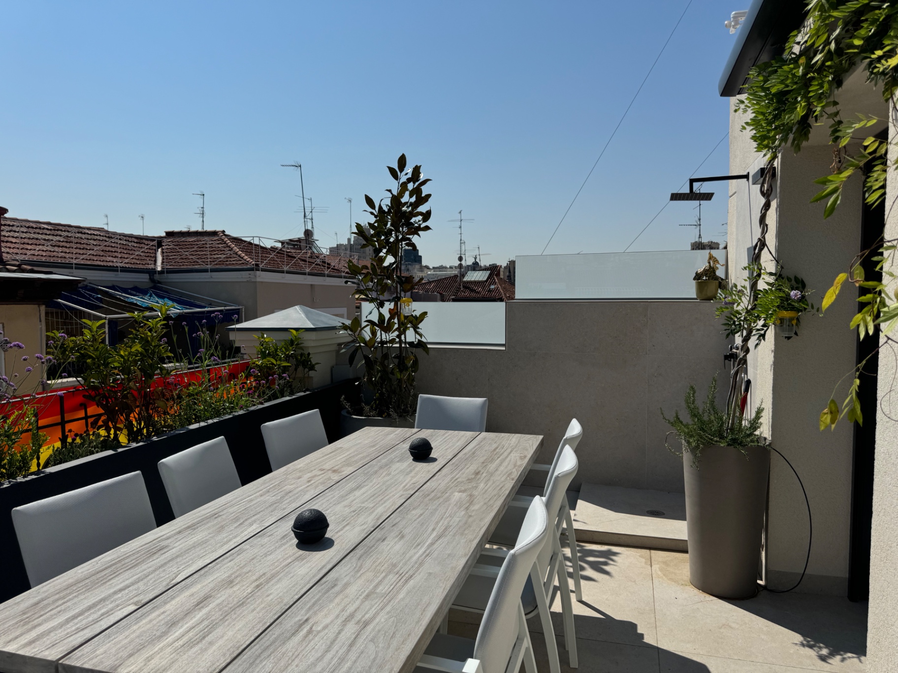 Mesa de comedor exterior para diez junto a un muro de piedra y trepadoras