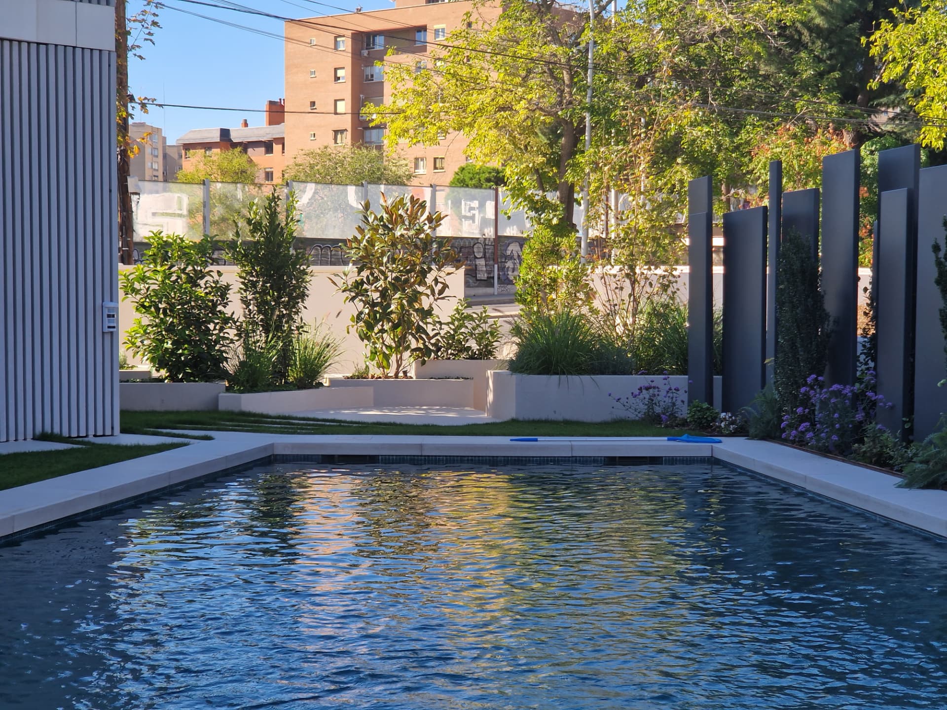 Piscina al atardecer enmarcada por plantación en capas y paneles oscuros escultóricos