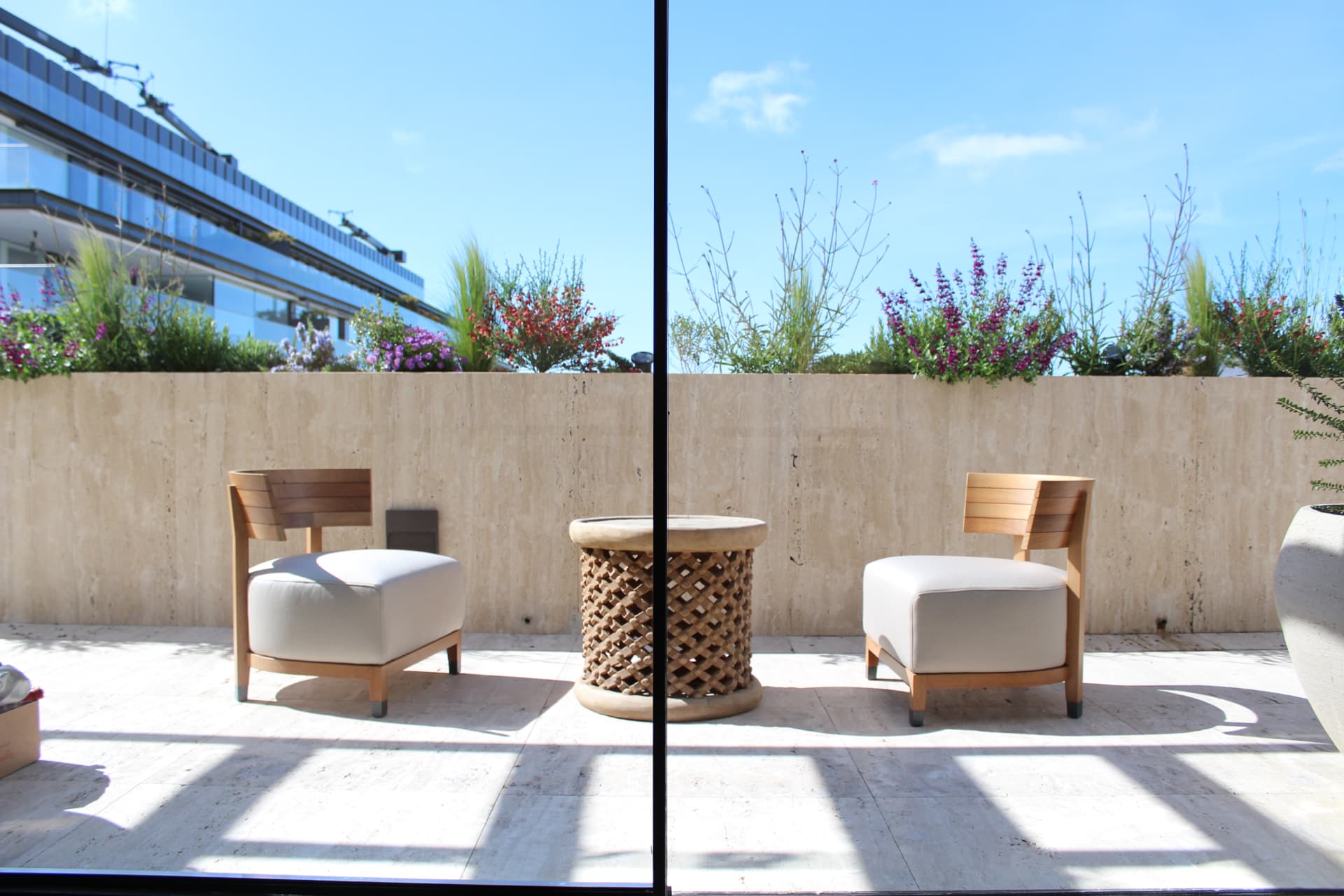 Salón exterior con butacas de madera y mesa de fibra bajo las jardineras en flor